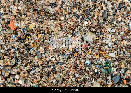 Close-up view of microplastic fragments scattered on beach, mixed with sand and pieces of glass, illustrating ocean and shore pollution, environmental Stock Photo