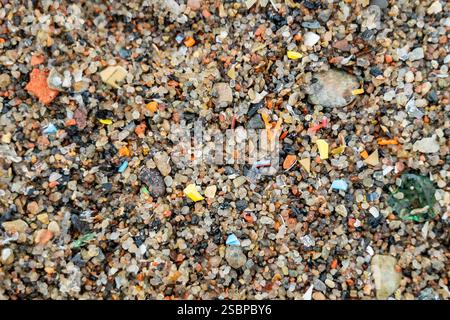 Close-up view of microplastic fragments scattered on beach, mixed with sand and pieces of glass, illustrating ocean and shore pollution, environmental Stock Photo