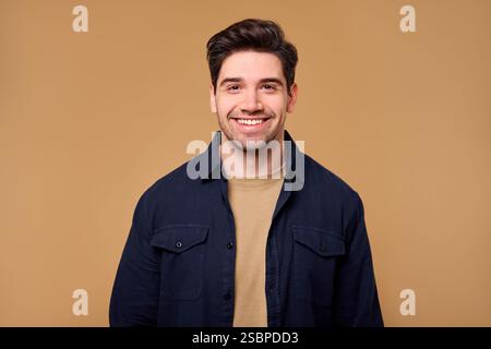 A cheerful young man with dark hair and a bright, warm smile is perfectly captured against a soft beige background, making it ideal for lifestyle phot Stock Photo