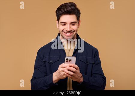 A joyful young man wearing a surprised expression has his eyes glued to his smartphone, his face radiating excitement. This image is perfect for theme Stock Photo