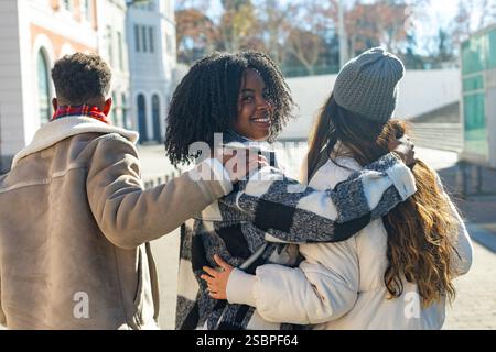 Three university students walking together in the city, embracing each other, during a sunny winter day Stock Photo