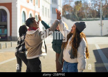 Group of cheerful multi ethnic friends giving high five while standing together in city celebrating success Stock Photo