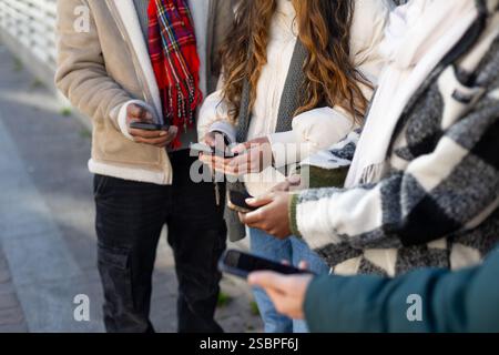 Close up of hands holding smartphones, showcasing winter fashion and mobile technology usage among young adults Stock Photo