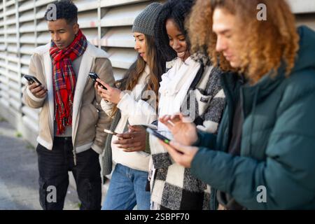 Group of diverse students using smartphones on a city street, sharing content and enjoying social media Stock Photo