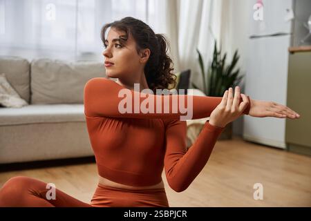 A beautiful young woman practices stretching exercises in her cozy living room setting. Stock Photo