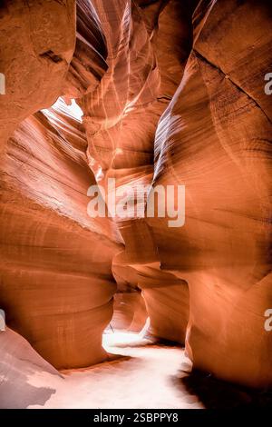 A narrow canyon with a light shining through it. The canyon is made of red rock. The light is coming from the sky Stock Photo