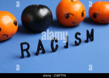 One black tangerine among orange ones and word Racism made with beads on blue background, closeup Stock Photo