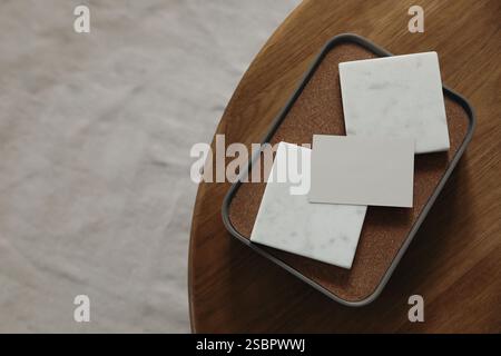 Blank business card and marble tiles mockups on round wooden coffee table. Blurred beige carpet. Elegant branding template. Flat lay, top view. Copy Stock Photo