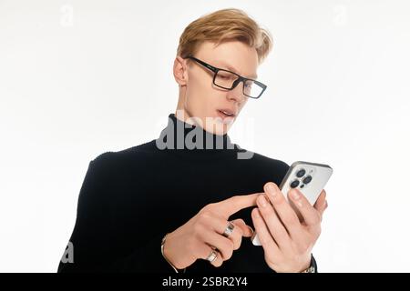 A stylish young man dressed in black checks his smartphone with concentration and interest. Stock Photo