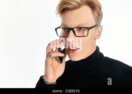Young man wearing glasses converses intently on his smartphone, showcasing modern style and focus. Stock Photo