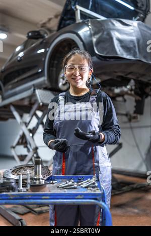 Young female mechanic wearing gloves and safety glasses working on a car in a professional auto repair shop Stock Photo