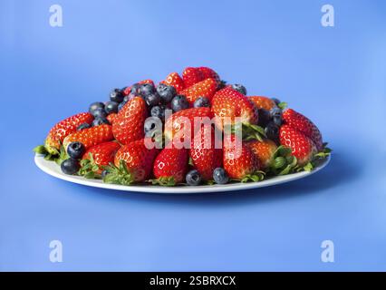 Three kinds of fresh berries on a white plate. on blau background Stock Photo