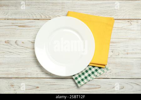Yellow and checkered napkins with empty plate on light wooden table, top view Stock Photo