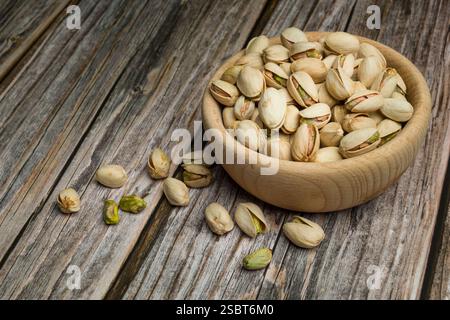 Bunch of pistachio nuts on wooden bowl on wooden table. Stock Photo