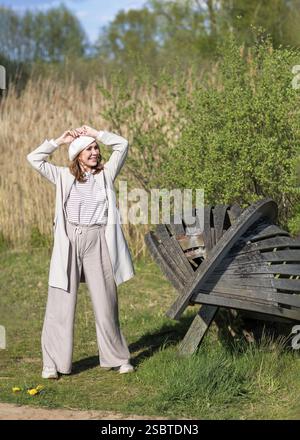 A beautiful middle-aged woman poses in nature on a sunny spring afternoon. The interplay of sunlight and shadows from the trees creates a stunning vis Stock Photo