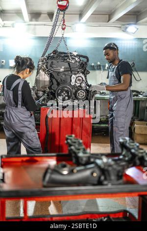 Two auto mechanics inspecting a car engine hanging from a chain hoist in a professional workshop Stock Photo