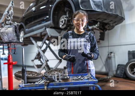 Confident young female mechanic wearing gloves and protective glasses, working on car parts in a professional auto repair shop Stock Photo