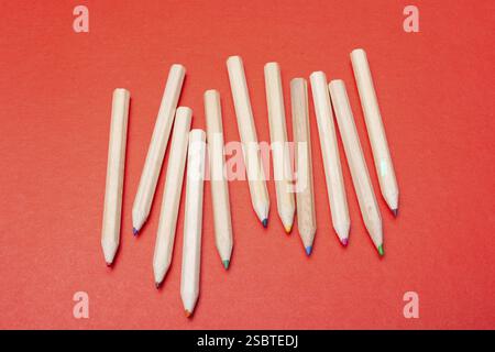 Colored pencils on red background. Many different colored pencils Stock Photo