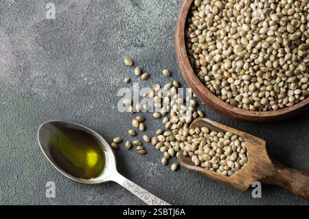 Hemp seed oil with heap of dried organic hemp seeds or cannabis plant seeds in spoon or bowl on rustic background, cannabis herb oil concept Stock Photo