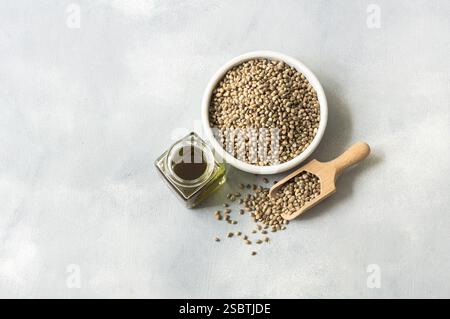 Hemp seed oil with heap of dried organic hemp seeds or cannabis plant seeds in spoon or bowl on rustic background, cannabis herb oil concept Stock Photo
