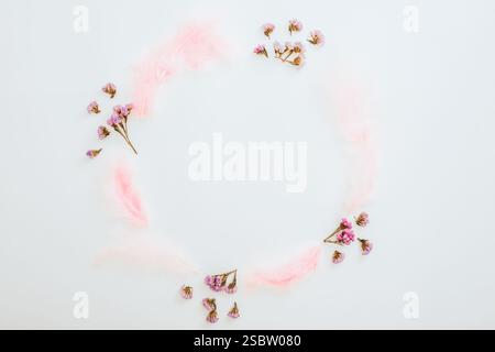 Round frame of pink flowers and feathers on white background. Flat lay Stock Photo