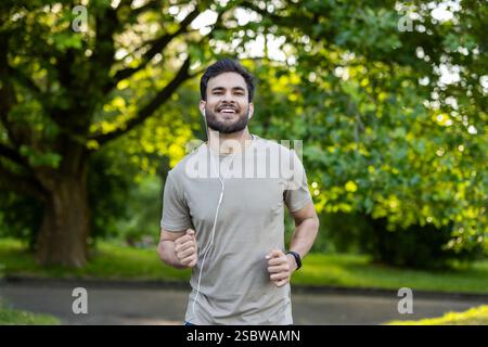Portrait of a smiling young Indian man wearing headphones doing sports and doing a morning jog in the park. Stock Photo