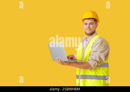 Male contractor using laptop on yellow background Stock Photo