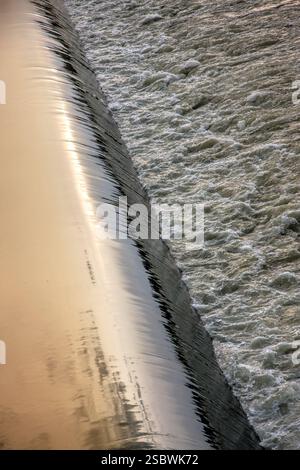 A large body of water with a reflection of the sky on the left side. The water is choppy and has white foam on the surface Stock Photo