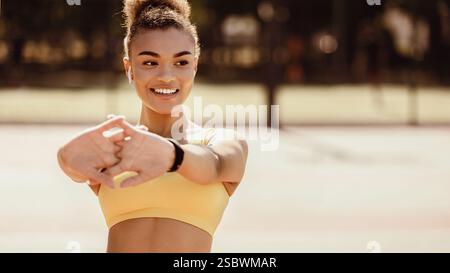 Sporty black woman in yellow sportswear stretching arms Stock Photo
