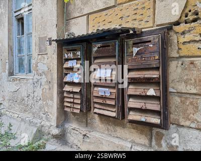 Group of old rusty mailboxes on the weathered stone wall of a residential building Stock Photo