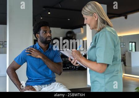 Female physical therapist talking to male patient and making notes Stock Photo