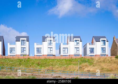 Modern seaside houses promenade view newbiggin by the sea lined up under a vibrant blue sky with fluffy clouds on a sandy beach northumberland uk Stock Photo