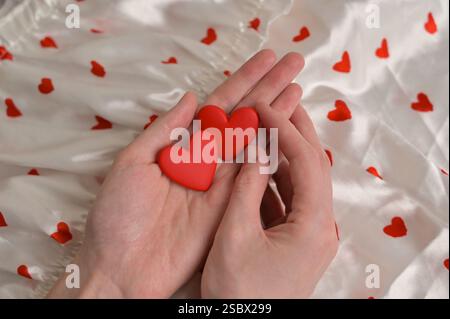 Woman holding couple of red earrings hearts shape in hands. White cloth with heart shape pattern background. Preparation to Valentine's Day Stock Photo