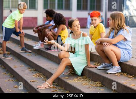 Happy tweenagers friends sitting on steps outdoors and chatting Stock Photo