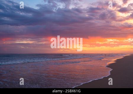 Intense sunset colors of red, purple, and orange fill the sky and reflect on the shoreline. Stock Photo