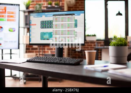 Empty workspace with desktop pc and big digital screen desk displaying business analytics data. Office table with nobody, has computer screen showing company statistics information in brick wall room. Stock Photo
