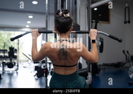 Strong female athlete exercising back muscles using lat pull down machine in modern fitness center, demonstrating her strength and dedication to healt Stock Photo