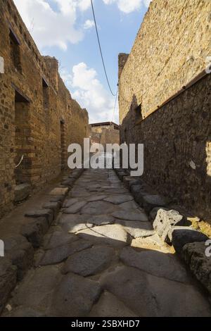 Long narrow street made of large grey smooth and worn lava stones with sidewalk plus remnants of old terracotta brick and stone wall structures and re Stock Photo