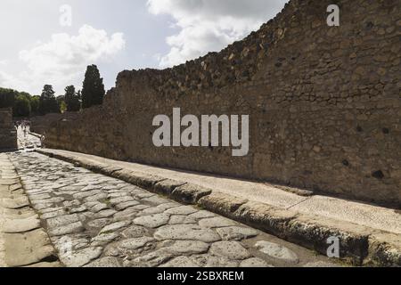 Long narrow stone sidewalk and street made of large grey smooth and worn lava stones plus remnant of old stone and terracotta brick wall structure at Stock Photo