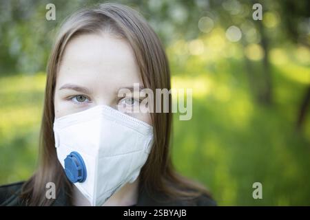 Woman wearing a protective mask in a green outdoor setting Stock Photo