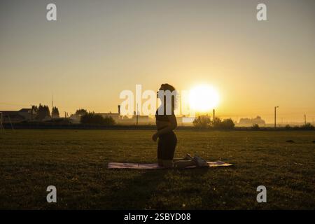 Person kneels on a yoga mat in a meditative pose during sunrise, creating a serene silhouette Stock Photo