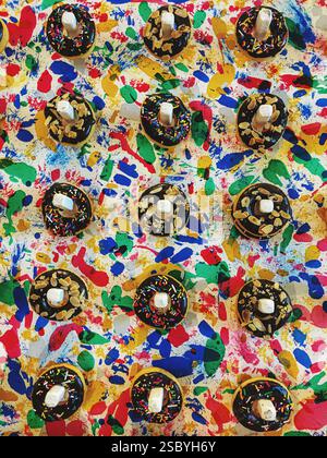 Variety of donuts with icing and chocolate toppings hanging against a multi-colored wall. Stock Photo