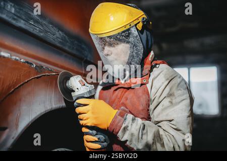 A worker in protective gear using a grinder on a vehicle Stock Photo