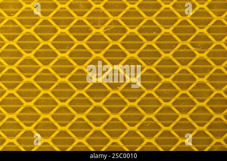 Macro texture of a reflective yellow, retro-reflective material, on a traffic sign, made up of a repetitive honeycomb-shaped pattern Stock Photo