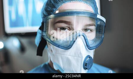 Individual wearing protective mask and goggles, blue medical attire Stock Photo