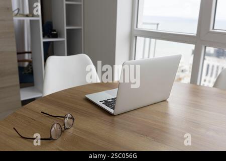 A wooden table with a laptop and glasses next to a white chair in a bright room Stock Photo