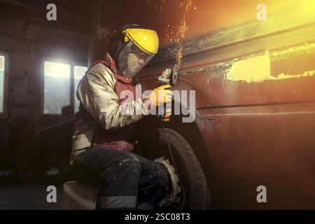 A person uses an angle grinder on automotive bodywork emitting sparks Stock Photo