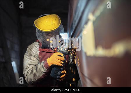 A worker uses an angle grinder with sparks flying in an industrial setting Stock Photo