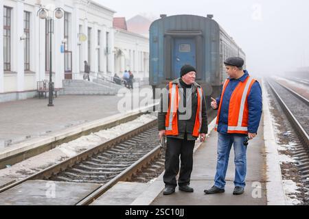 January 19, 2015, Romny, Ukraine: Two railway workers in orange protective vests are chatting on a foggy platform near an old blue train Stock Photo