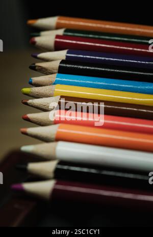 Perspective view of Multi colored pencils or wooden crayons to each other arranged in a neat row on dark background. The arrangement of the colors pen Stock Photo